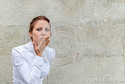 Smiling woman blowing air kiss sign gesture on urban wall background with copy space Stock Photo