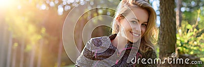 Attractive smiling young blond woman, wearing sportswear, relaxing after workout in a forest. Stock Photo