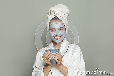 Attractive spa woman in cosmetic face mask drinking coffee in blue mug on gray background Stock Photo
