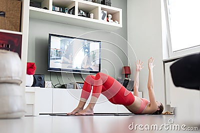 Attractive sporty woman working out at home, doing pilates exercise in front of television in her small studio Stock Photo