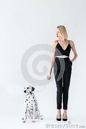 attractive stylish blonde woman in black clothes holding dalmatian dog leash Stock Photo