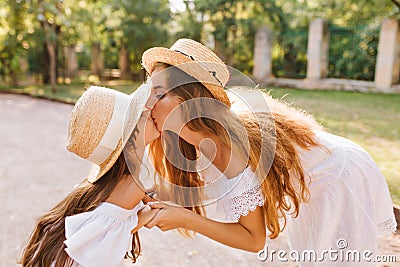 Attractive stylish woman bent over to the daughter to kiss her. Cute outdoor portrait of sweet long-haired girl in Stock Photo
