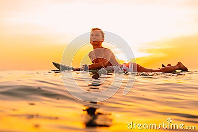 Attractive surfer woman on a surfboard in ocean. Surfgirl at sunset Stock Photo