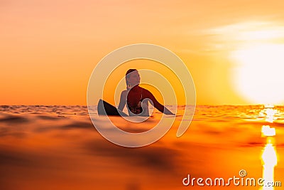 Attractive surfer woman on a surfboard in ocean. Surfgirl at sunset Stock Photo