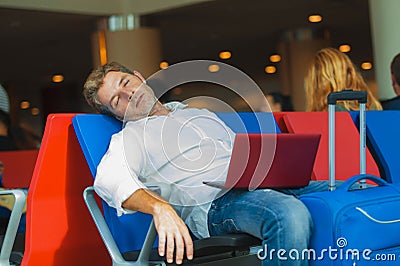 Attractive and tired traveler man with luggage taking a nap sleeping while working with laptop computer waiting for flight at Stock Photo