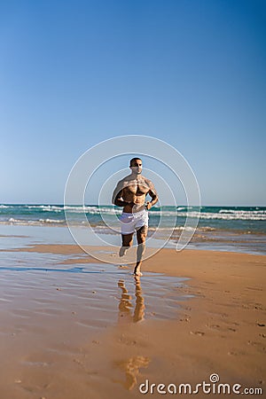 An attractive topless man with tattoos running on a beach next to a sea Stock Photo