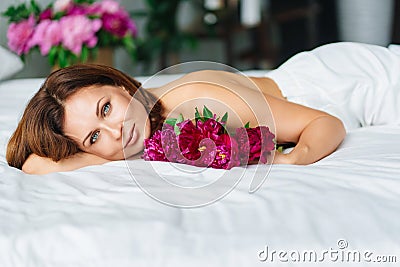 attractive topless woman with a bouquet of peonies on the bed. Stock Photo