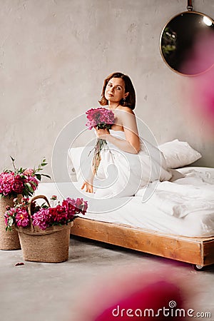 attractive topless woman with a bouquet of peonies in a blanket on the bed. Stock Photo