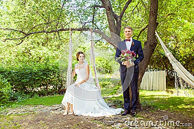 Attractive wife sitting on swing near husband at summer garden Stock Photo