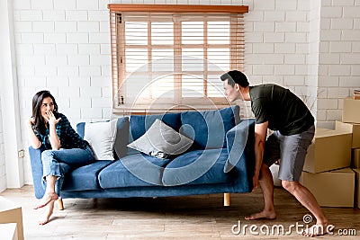 Attractive wife is teasing her husband, Which is moving a sofa in their new home where they are relocation Stock Photo