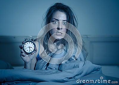 Attractive woman in bed showing alarm clock to camera feeling worried, stressed and sleepless Stock Photo