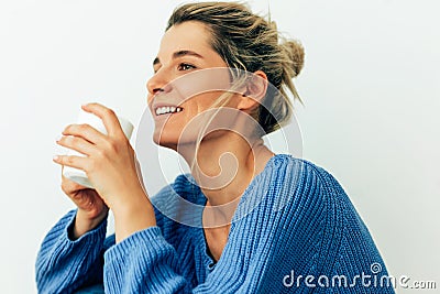 Attractive woman dressed in cozy knitted blue sweater with a mug. Beautiful young woman drinking hot beverage at home. Charming Stock Photo