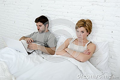 Attractive woman feeling upset unsatisfied and frustrated in bed with his husband while the man work on computer laptop ignoring h