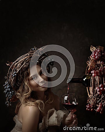 Attractive woman with glass of red wine in wine cellar . Vine wreath with blue grapes on a head. Red wine is poured from a bottle Stock Photo