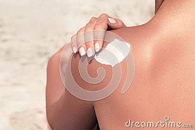 Attractive woman with healthy skin applying sunscreen to shoulder wearing white sun hat Stock Photo