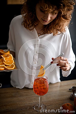 Attractive woman holds tweezers with slice of orange over glass with drink. Stock Photo