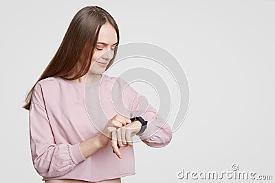 Attractive woman looks at smartwatch, checks calories or pulse, wears casual oversized sweater, has dark staight hair, on Stock Photo