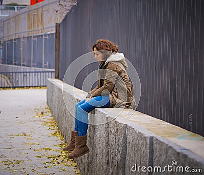 Depressed young woman sitting on urban city street overwhelmed a Stock Photo