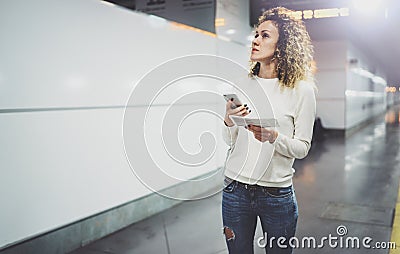 Attractive woman on transit using smartphone while walking with hand luggage backpack in train station or airpot going Stock Photo