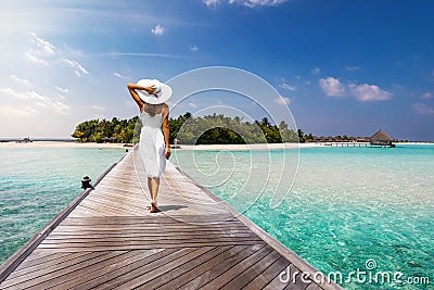 Attractive woman walks over a wooden jetty towards a tropical island Stock Photo