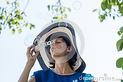 Attractive woman in a wide brimmed sunhat blowing bubbles Stock Photo