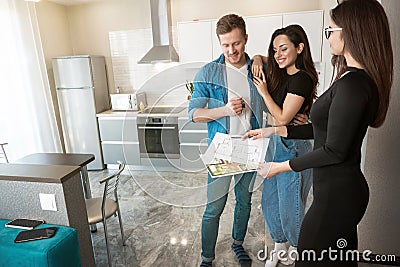 Attractive woman realtor property manager showing plannings of new appartment on sale to young beautiful couple husband and wife Stock Photo