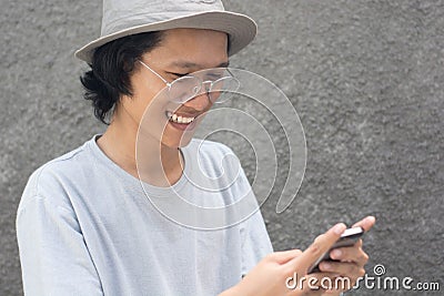 Attractive young asian man with hat and glasses using smarphone and smiling Stock Photo