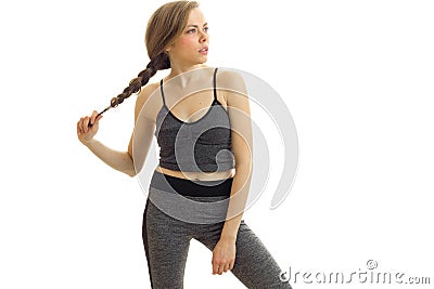 Attractive young blonde poses on cam in a gray sport suit and keeps hand pigtail Stock Photo