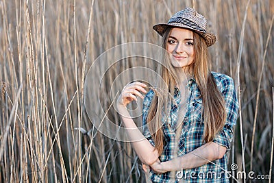 Attractive young blonde woman in blue plaid shirt straw hat enjoying her time on wild bush hard noon sun. Stock Photo