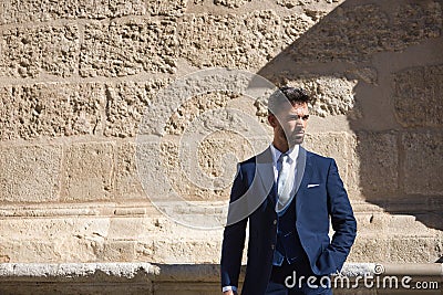 Attractive young businessman with beard and suit, posing next to a stone wall. Concept beauty, fashion, success, achiever, trend Stock Photo