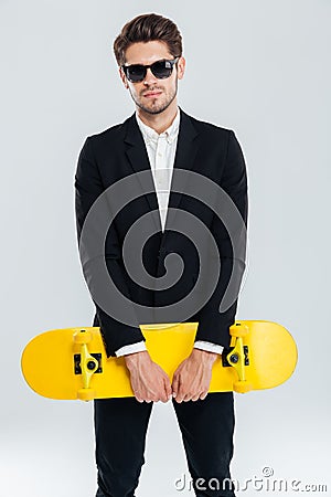 Attractive young businessman in black suit holding yellow skateboard Stock Photo