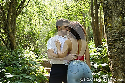 Attractive young couple in love, looking into each other`s eyes, close faces about to kiss, in an outdoor park, surrounded by Stock Photo