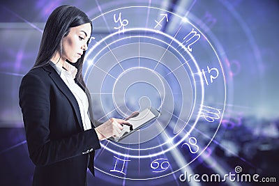 Attractive young european businesswoman with tablet and abstract astrological wheel hologram on blurry office interior background Stock Photo