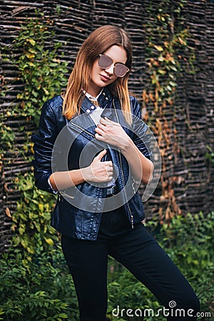 Attractive, young, fashionably dressed woman on the background of a wicker fence made of branches Stock Photo