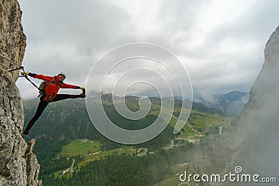 Attractive young female mountain climber on a Via Ferrata in the Dolomites in a crazy stretching pose Stock Photo