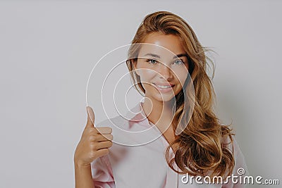 Attractive young girl with beautifully styled hair showing thumb up, standing over grey Stock Photo