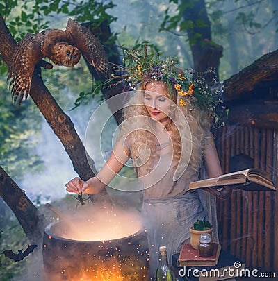 Attractive young girl with blond hair with an amazing lush wreath on her head in the forest, preparing potion in cauldro Stock Photo