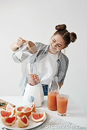 Attractive young girl smiling adding water in blender with grapefruit pieces and rosemary. Healthy diet food nutrition. Stock Photo