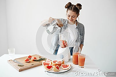 Attractive young girl smiling adding water in blender with grapefruit pieces and rosemary. Healthy diet food nutrition. Stock Photo