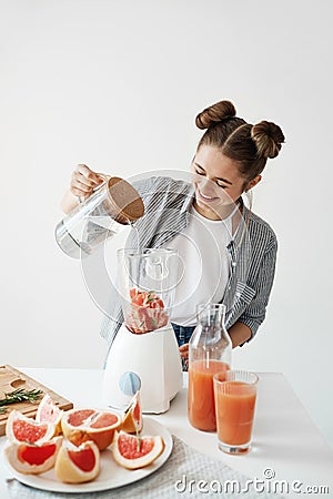 Attractive young girl smiling adding water in blender with grapefruit pieces and rosemary. Healthy diet food nutrition. Stock Photo