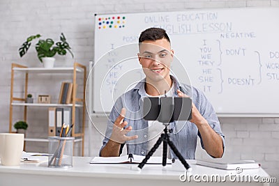 Attractive young man explains english rules and gestures on webcam in class Stock Photo