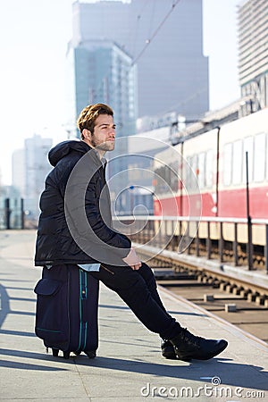 Attractive young man sitting and waiting for train at station Stock Photo