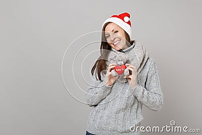 Attractive young Santa girl in gray sweater, scarf Christmas hat holding teddy bear plush toy isolated on grey Stock Photo