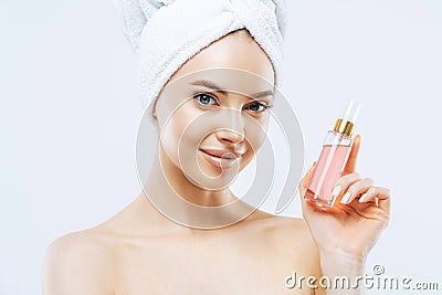Attractive young woman applies parfum, enjoys pleasant scent, stands with naked shoulders, has natural makeup, healthy skin, Stock Photo