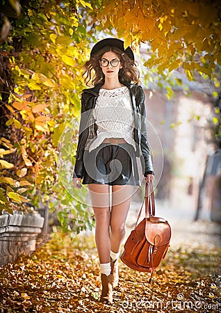 Attractive young woman in an autumnal shot outdoors. Beautiful fashionable school girl posing in park with faded leaves around Stock Photo