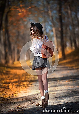 Attractive young woman in an autumnal shot outdoors. Beautiful fashionable school girl posing in park with faded leaves around Stock Photo