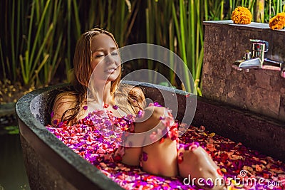 Attractive Young woman in bath with petals of tropical flowers and aroma oils. Spa treatments for skin rejuvenation Stock Photo