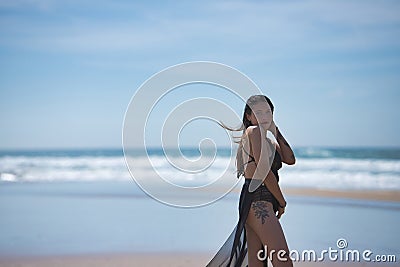 Attractive young woman, blue eyes, wearing black swimsuit and sarong, lonely and quiet, walking on the beach. Concept tranquility Stock Photo