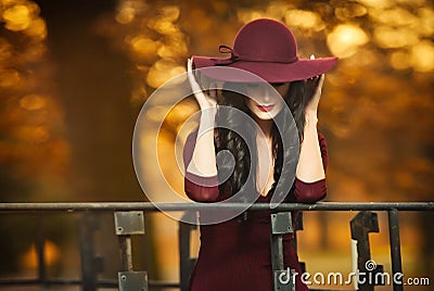 Attractive young woman with burgundy colored large hat in autumnal fashion shot. Beautiful mysterious lady covering the face Stock Photo