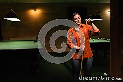 Attractive young woman chalking billiard cue while standing near pool table Stock Photo